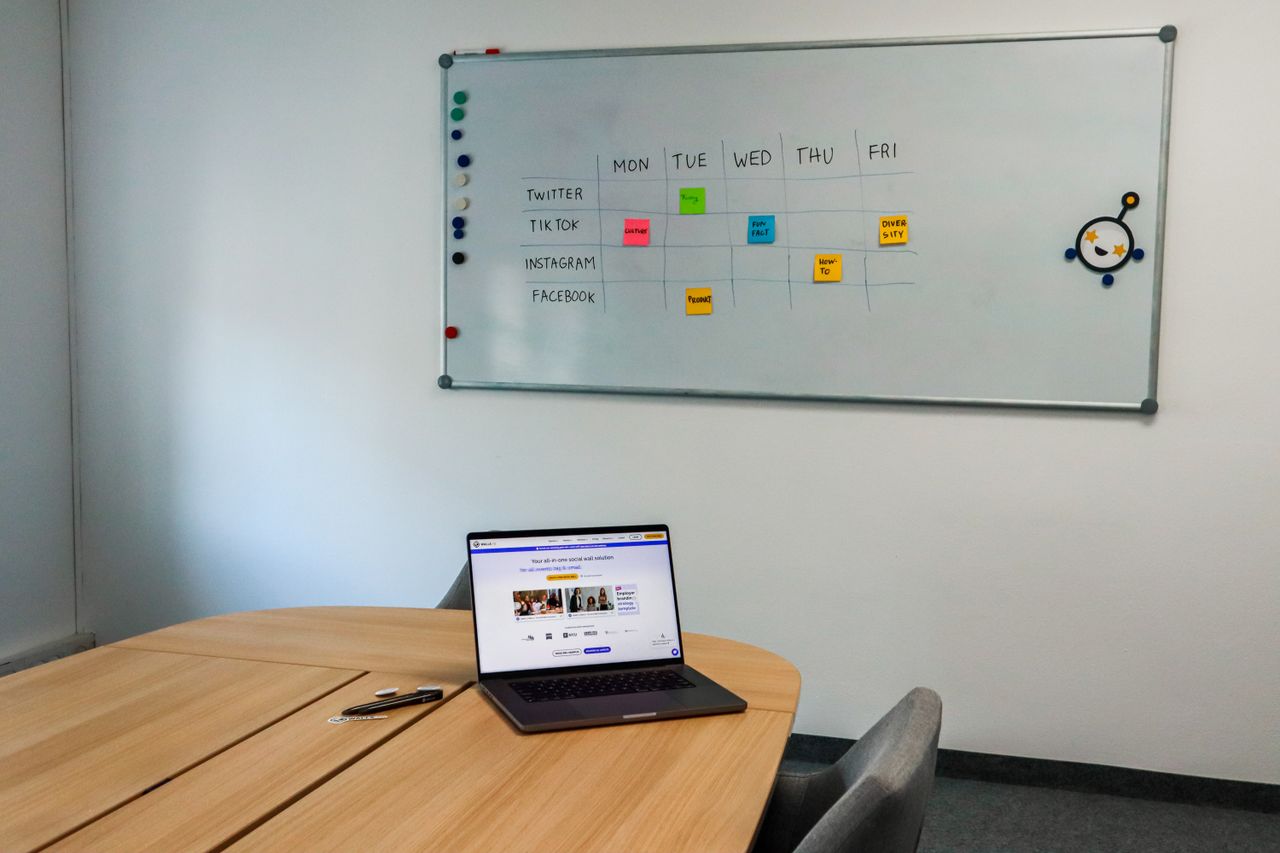 why-choose-us Office setup featuring a conference table, laptop, and organized whiteboard schedule, highlighting a tech-driven workspace.